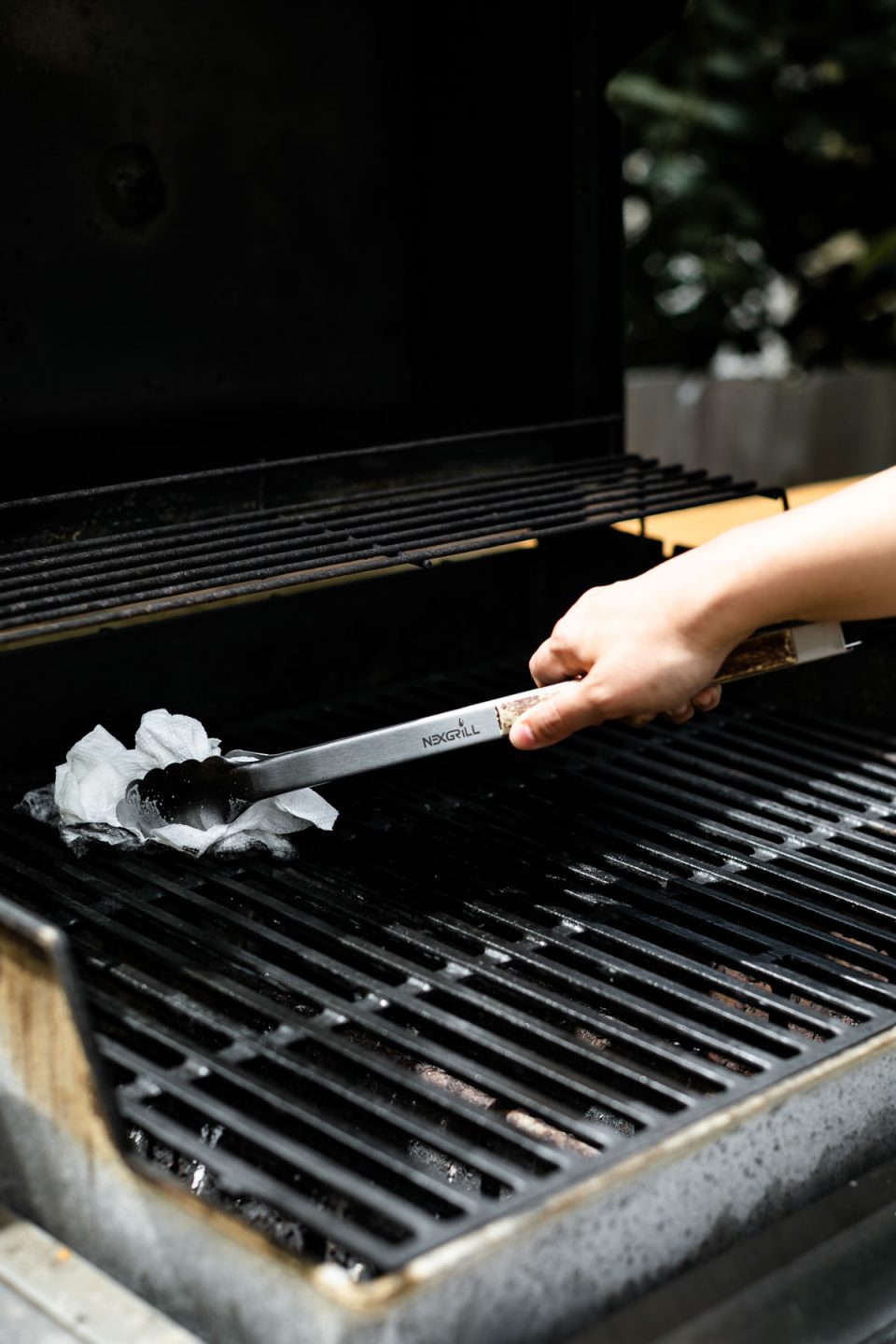 Preparing the grill to grill turkey burgers. A woman's hand reaches into the photo with grill tongs holding lightly greased paper towel to grease the grill grates of a gas grill.