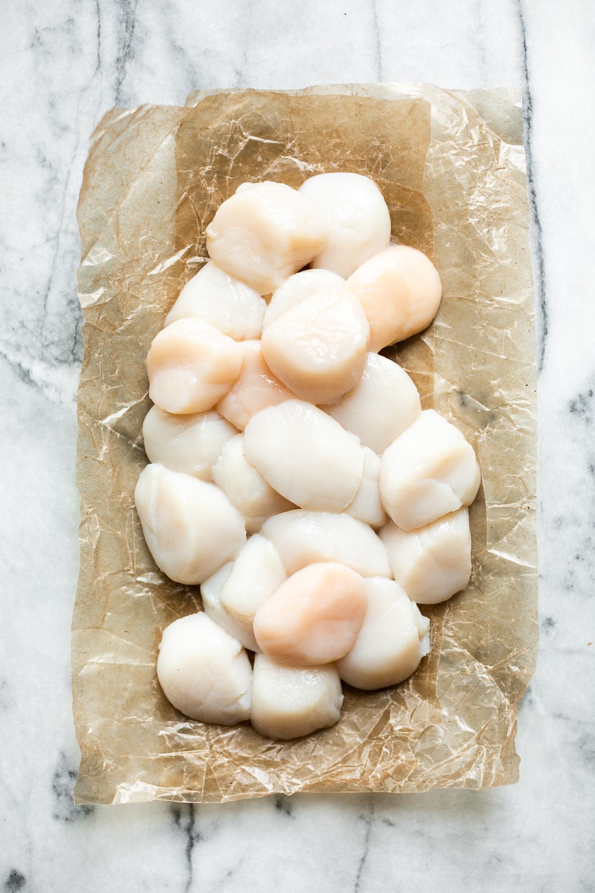 Cleaned sea scallops sitting atop parchment paper on a white marble surface.
