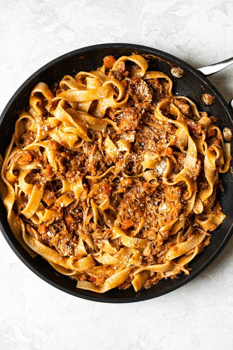 Braised pork ragu tossed into pappardelle pasta in a skillet.