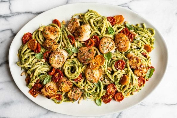 Seared Scallops and Kale Pesto Pasta on a white serving platter garnished with fresh basil leaves. The platter sits on a grey and white marble surface.