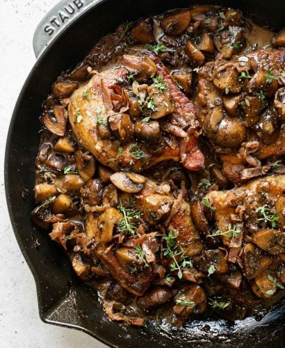 Pork marsala with mushrooms & creamy marsala sauce in large gray Staub skillet. The pork chops are topped with caramelized mushrooms, crispy prosciutto & fresh thyme. The skillet sits atop a white surface.