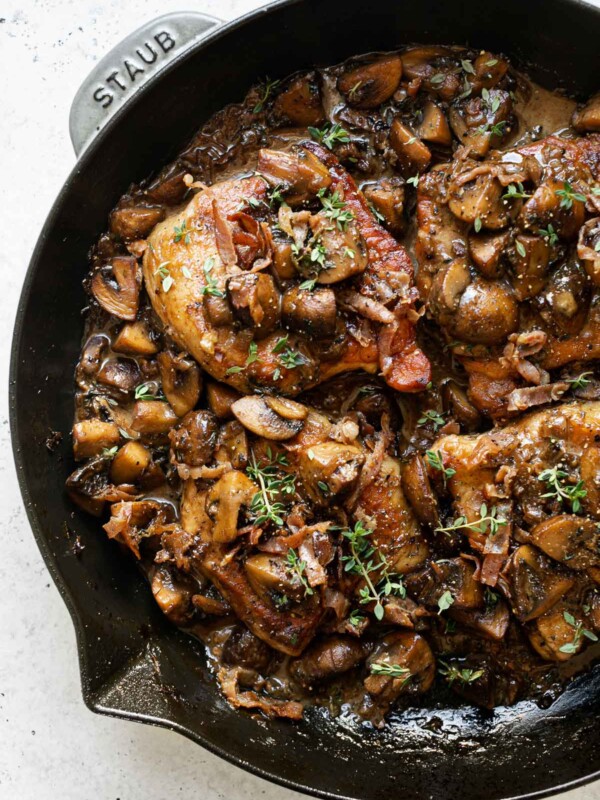 Pork marsala with mushrooms & creamy marsala sauce in large gray Staub skillet. The pork chops are topped with caramelized mushrooms, crispy prosciutto & fresh thyme. The skillet sits atop a white surface.