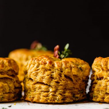 Side angle of a row of pumpkin biscuits. The biscuits have a pecan & fresh herbs inserted in their tops, making the biscuits look like little pumpkins.