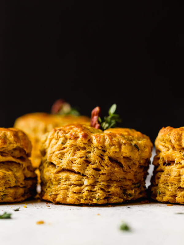Side angle of a row of pumpkin biscuits. The biscuits have a pecan & fresh herbs inserted in their tops, making the biscuits look like little pumpkins.