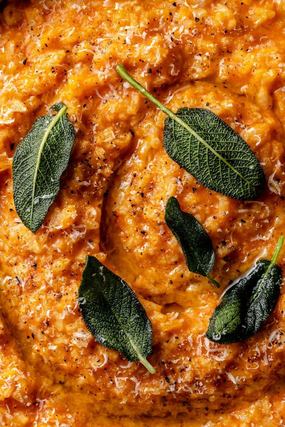 Close up of creamy pumpkin risotto topped with crispy fried sage leaves & finely grated parmesan.