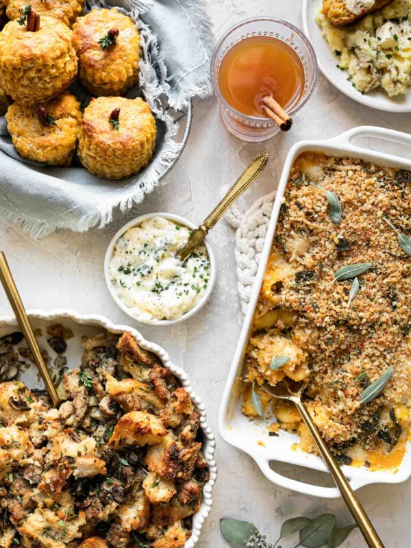 Sidesgiving tablescape, with pumpkin biscuits, pumpkin mac & cheese, & stuffing all placed in serving dishes shown on a neutral backdrop.