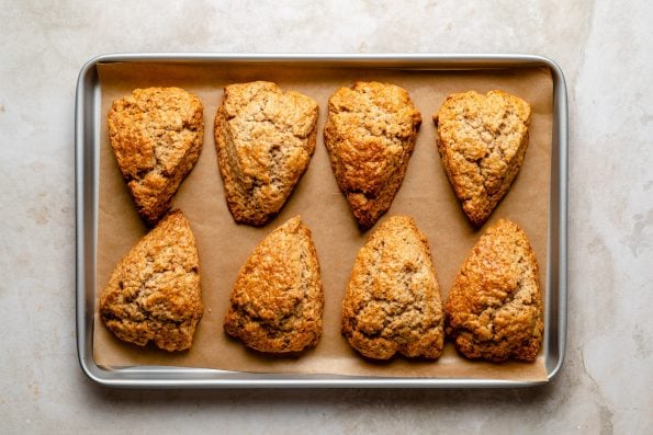 Baked chai spice scones arranged on a parchment-lined baking sheet atop a creamy marble surface.