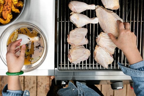 Woman's hands reaching into the frame, removing chicken from apple cider brine & placing on grill grates.