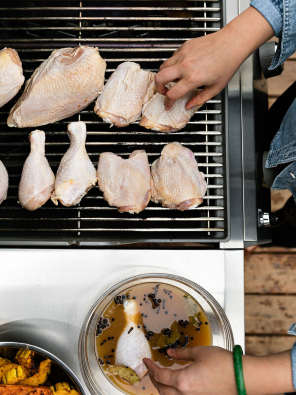 Woman's hands reaching into the frame, removing chicken from apple cider brine & placing on grill grates.
