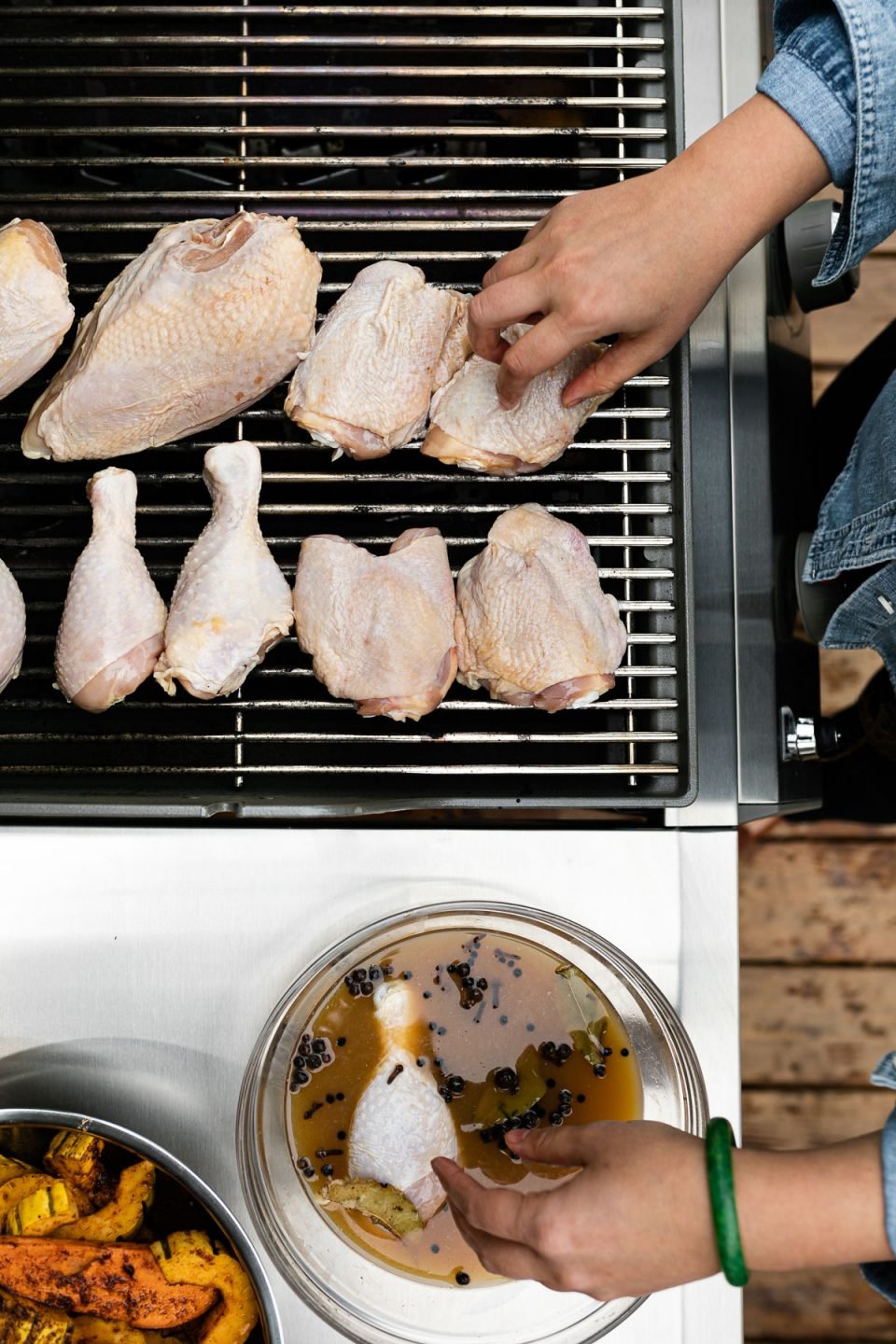 Woman's hands reaching into the frame, removing chicken from apple cider brine & placing on grill grates.