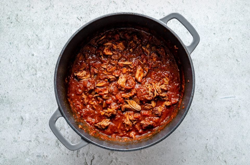 Braised lamb ragu in a large Dutch oven atop a light blue surface.