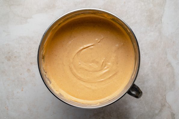 Creamy pumpkin cheesecake filling shown in a large stainless steel mixing bowl.