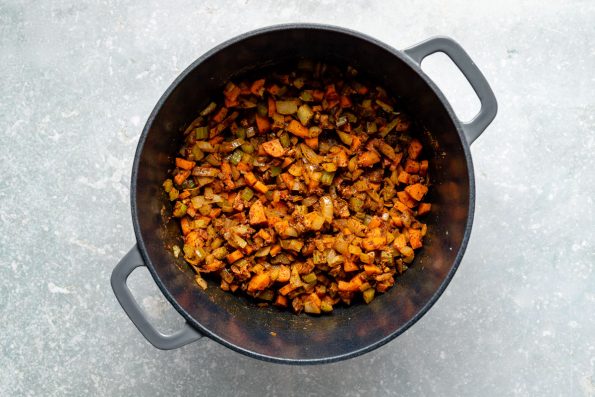 How to make lentil soup: Spices added to softened mirepoix shown in a large gray dutch oven atop a light blue surface.