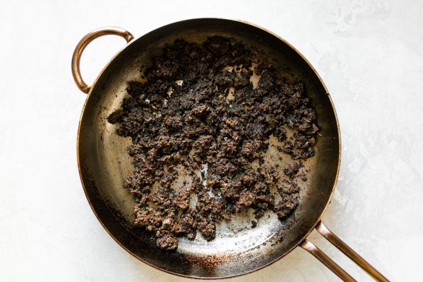 Mushroom duxelles in a large skillet atop a white surface.