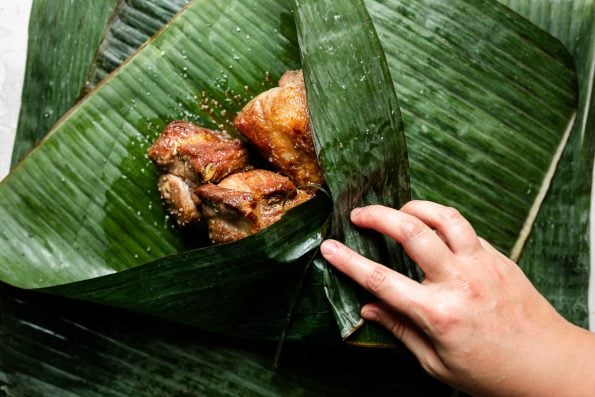 A woman's hands folding banana leaf around seasoned browned pork.