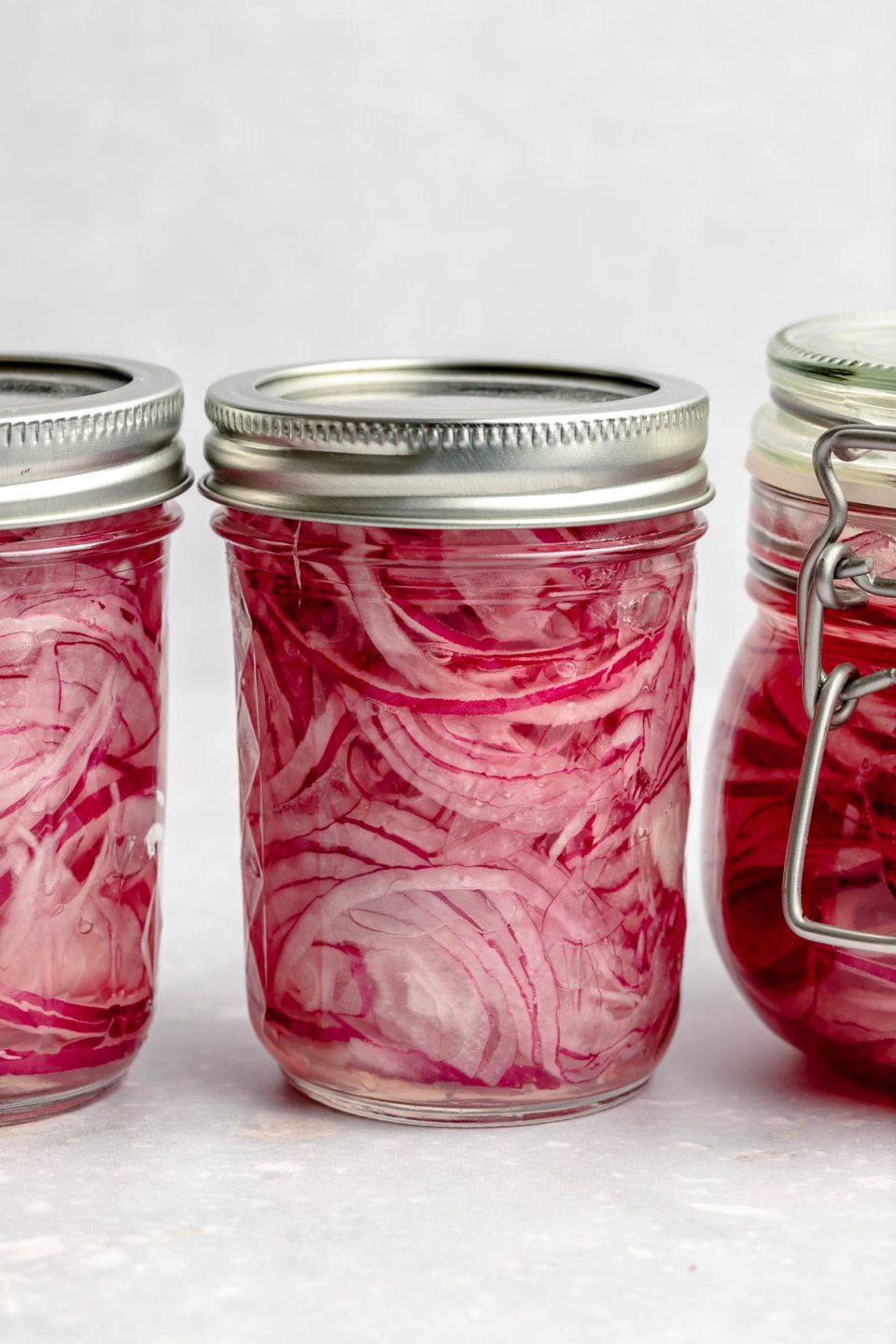 A profile shot of three mason jars full of quick & easy pickled red onions.