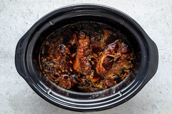 How to make Slow cooked lamb shoulder with balsamic, rosemary, and garlic, step 2: Slow cook the lamb. Lamb slow cooked in a braising liquid until fall-apart tender rests inside a slow cooker. The slow cooker sits atop a grey textured surface.