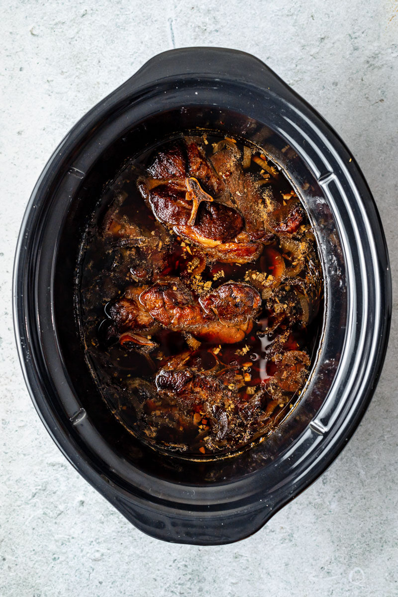 How to make Slow cooked lamb shoulder with balsamic, rosemary, and garlic, step 2: Slow cook the lamb. Lamb slow cooked in a braising liquid until fall-apart tender rests inside a slow cooker. The slow cooker sits atop a grey textured surface.