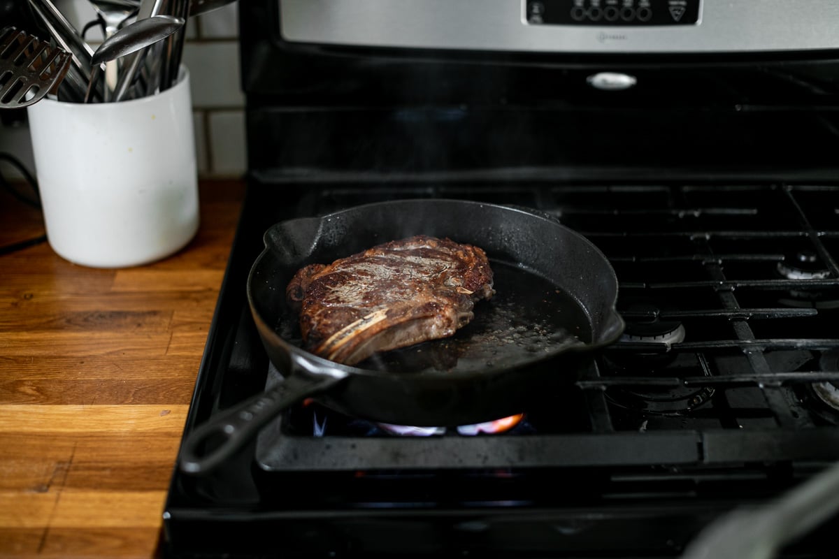 A photo of a seared steak in a cast iron skillet over high flame heat on a gas range.