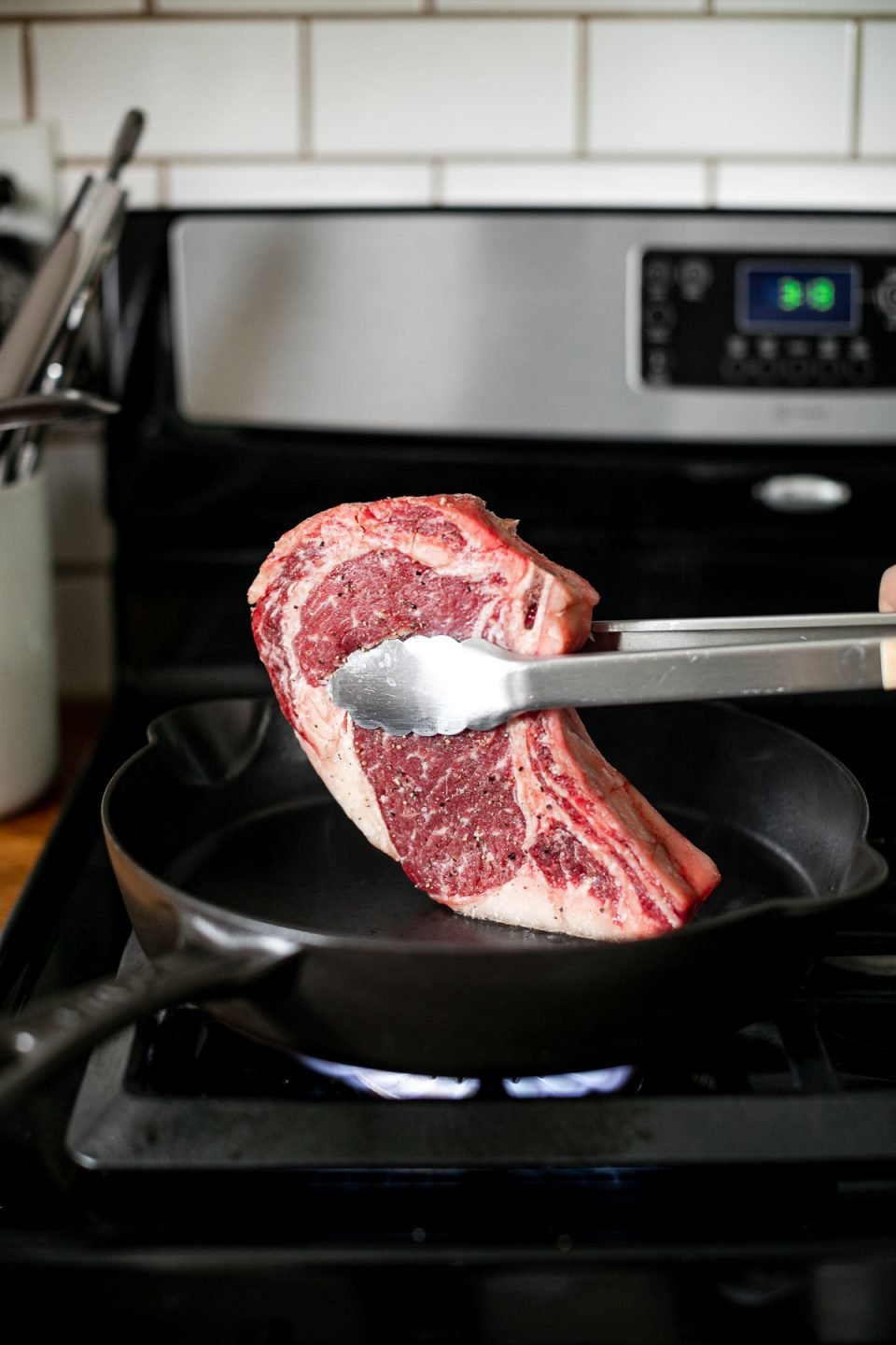 A side angle photo of rendering fat cap off of bone-in ribeye in a large black skillet over stove burner.