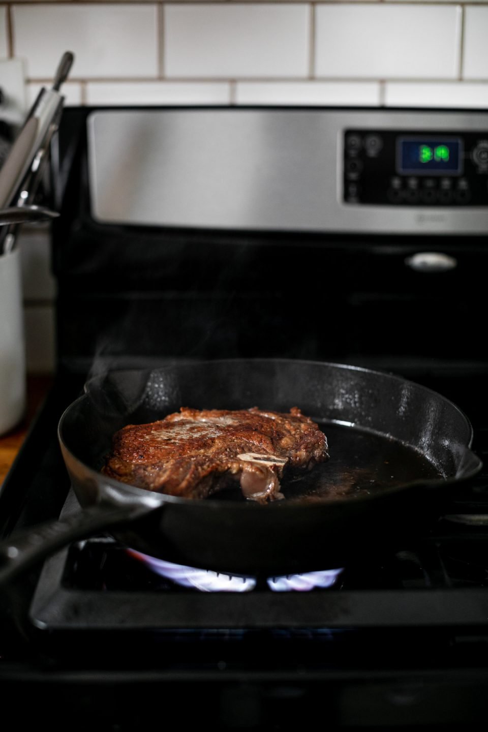 A photo of a seared steak in a cast iron skillet over high flame heat on a gas range. 