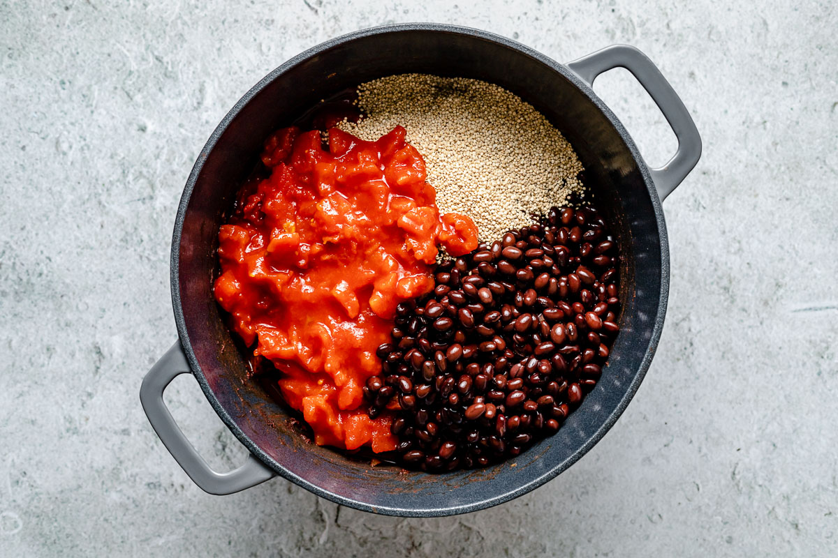 How to make Sweet Potato Quinoa Chili - Step 3: Diced tomatoes, quinoa & black beans added a large gray Dutch oven, which sits atop a light blue surface.