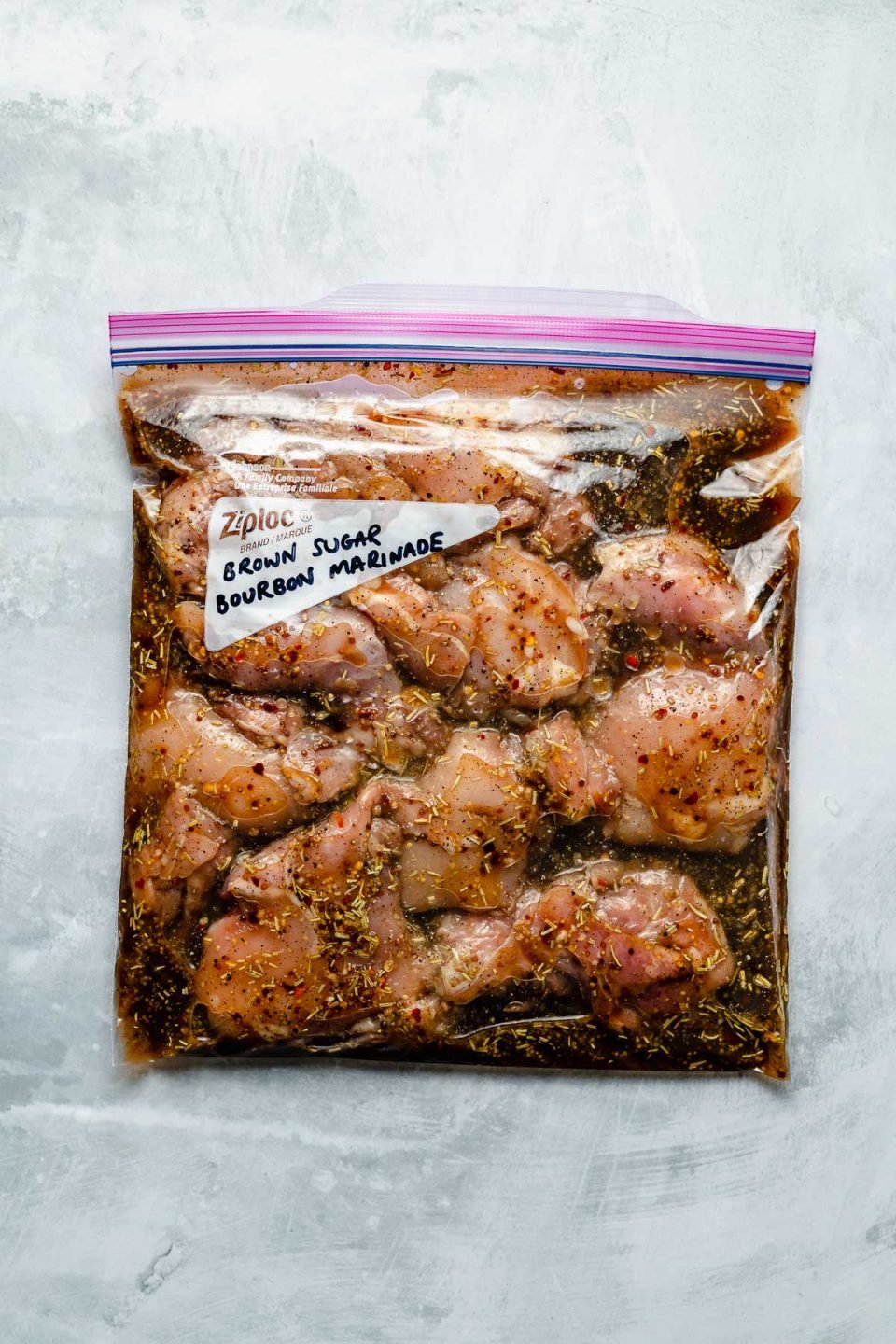 Chicken thighs in a Ziploc bag, marinating in Brown Sugar Bourbon marinade. The bag sits atop a light blue surface. “Brown Sugar Bourbon Marinade" is penned in the bag's memo area.