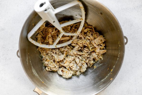 How to make Chicken Carnitas, Step 4: Shredded chicken in bowl of stand mixer with paddle attachment, which sits atop a white surface.