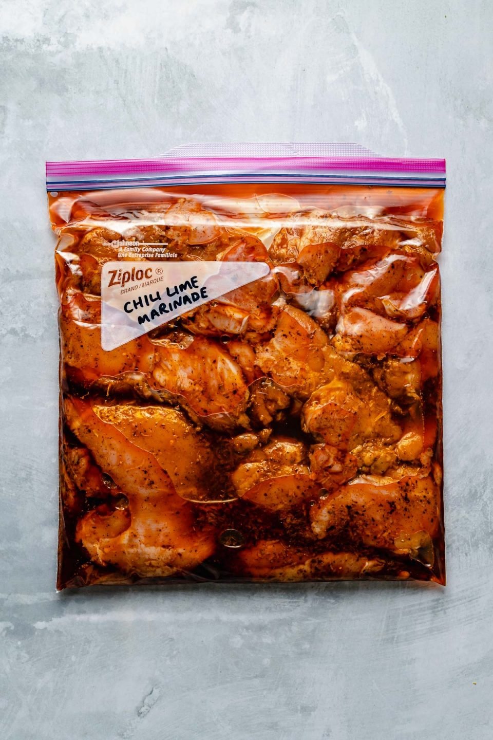 Chicken thighs in a Ziploc bag, marinating in Chili Lime marinade. The bag sits atop a light blue surface. “Chili Lime Marinade" is penned in the bag's memo area.