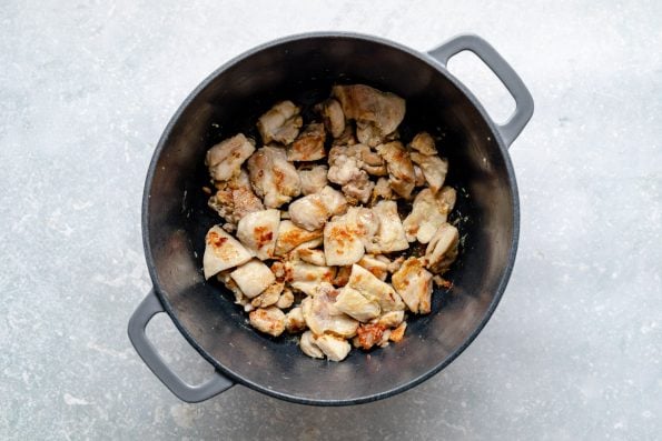 How to make Thai green curry, Step 5: Gingery chicken sears in a large Dutch oven. The Dutch oven sits atop a light blue surface.