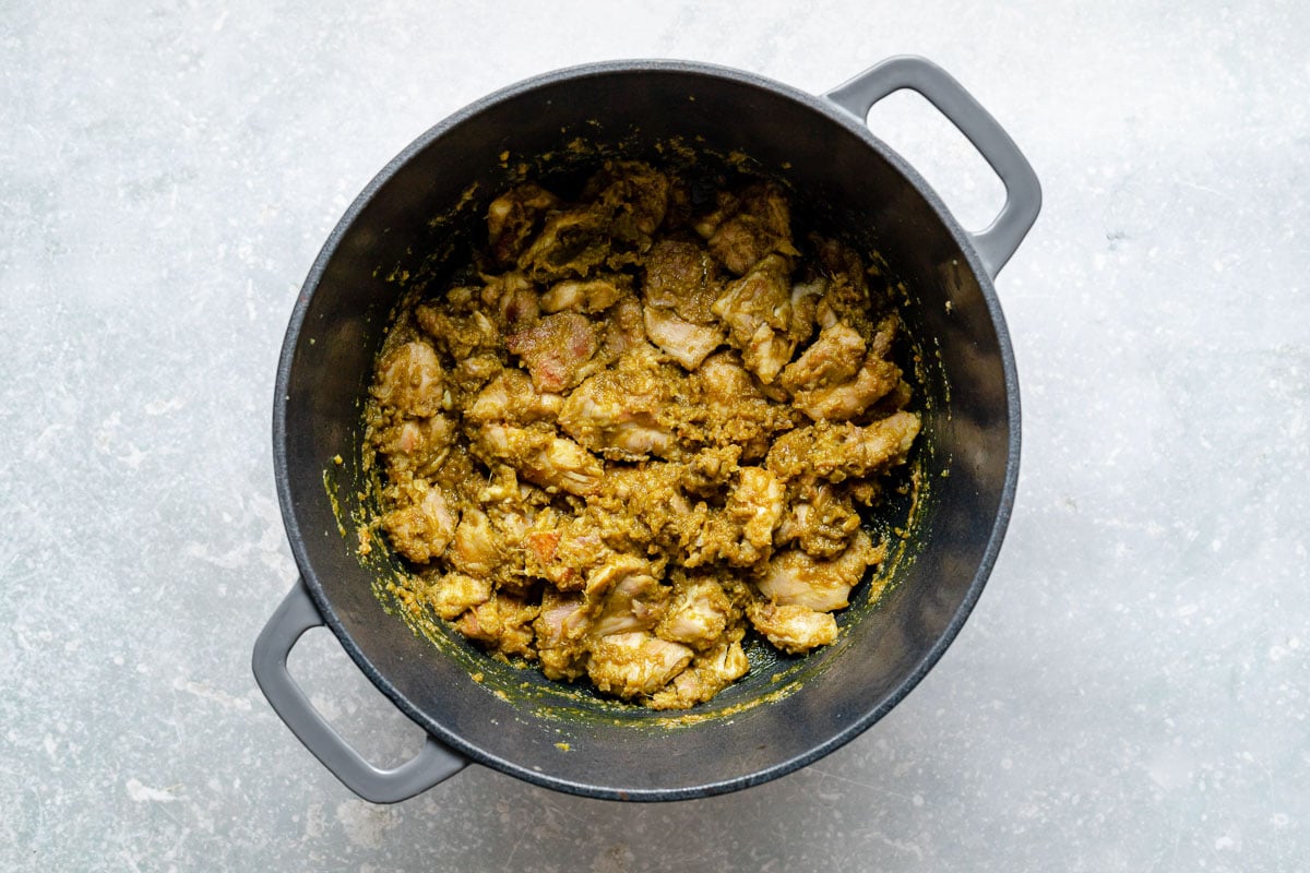 How to make Thai green curry, Step 6: Browned chicken coated in green curry paste in a large Dutch oven. The Dutch oven sits atop a light blue surface.