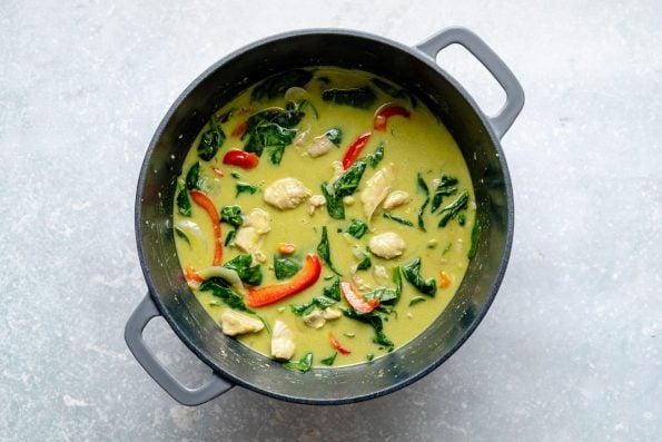 Thai green chicken curry in a large Dutch oven atop a light blue surface.