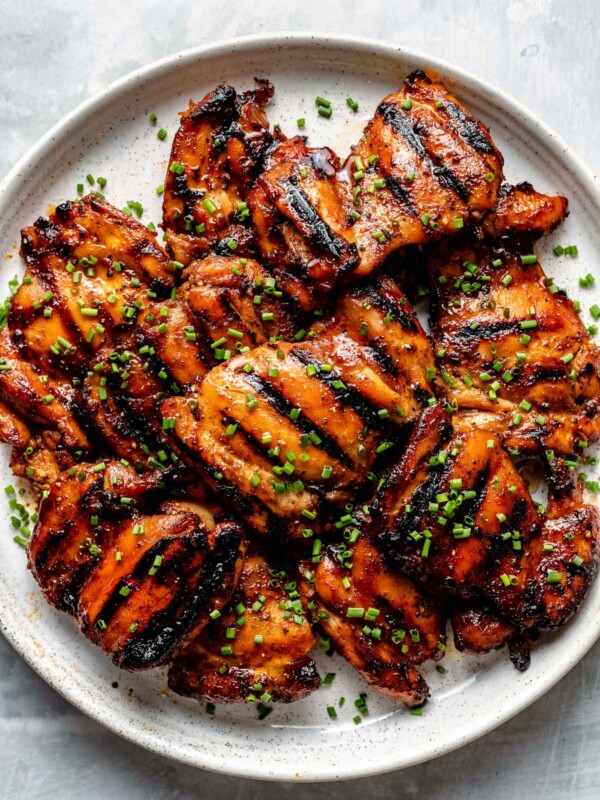 Grilled all-purpose marinated chicken thighs shown on a white speckled plate atop a light blue surface. The chicken is garnished with diced chives.