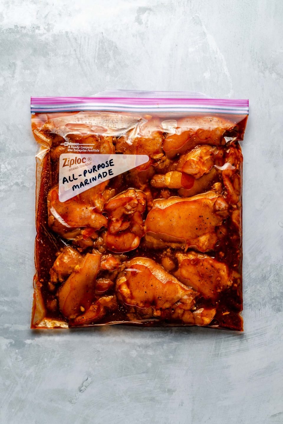 Chicken thighs in a Ziploc bag, marinating in All-Purpose marinade. The bag sits atop a light blue surface. “All-Purpose Marinade" is penned in the bag's memo area.