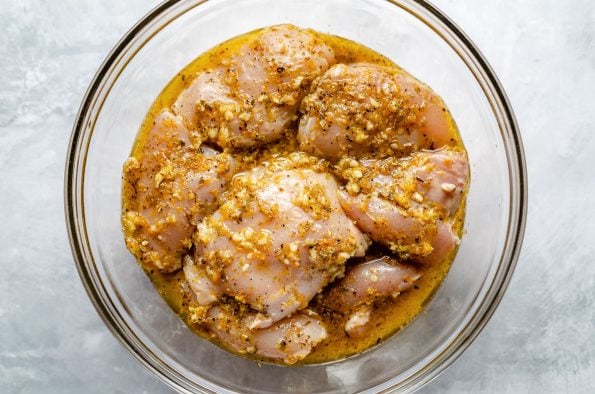 Chicken thighs in mojo marinade in a large glass bowl atop a light blue surface.