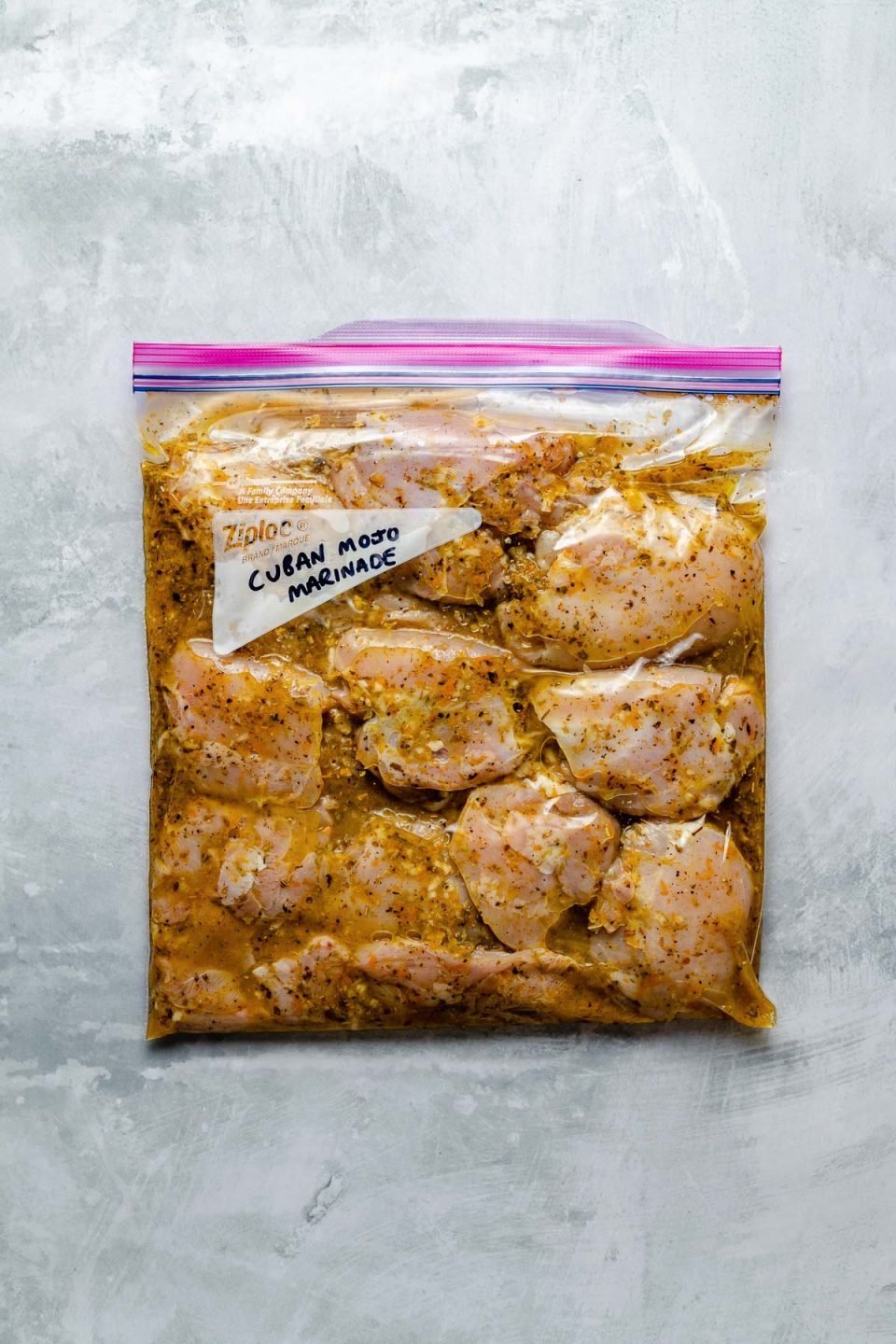 Chicken thighs in mojo marinade in a Ziploc bag atop a light blue surface. "Cuban Mojo Marinade" is written in the bag's memo space.