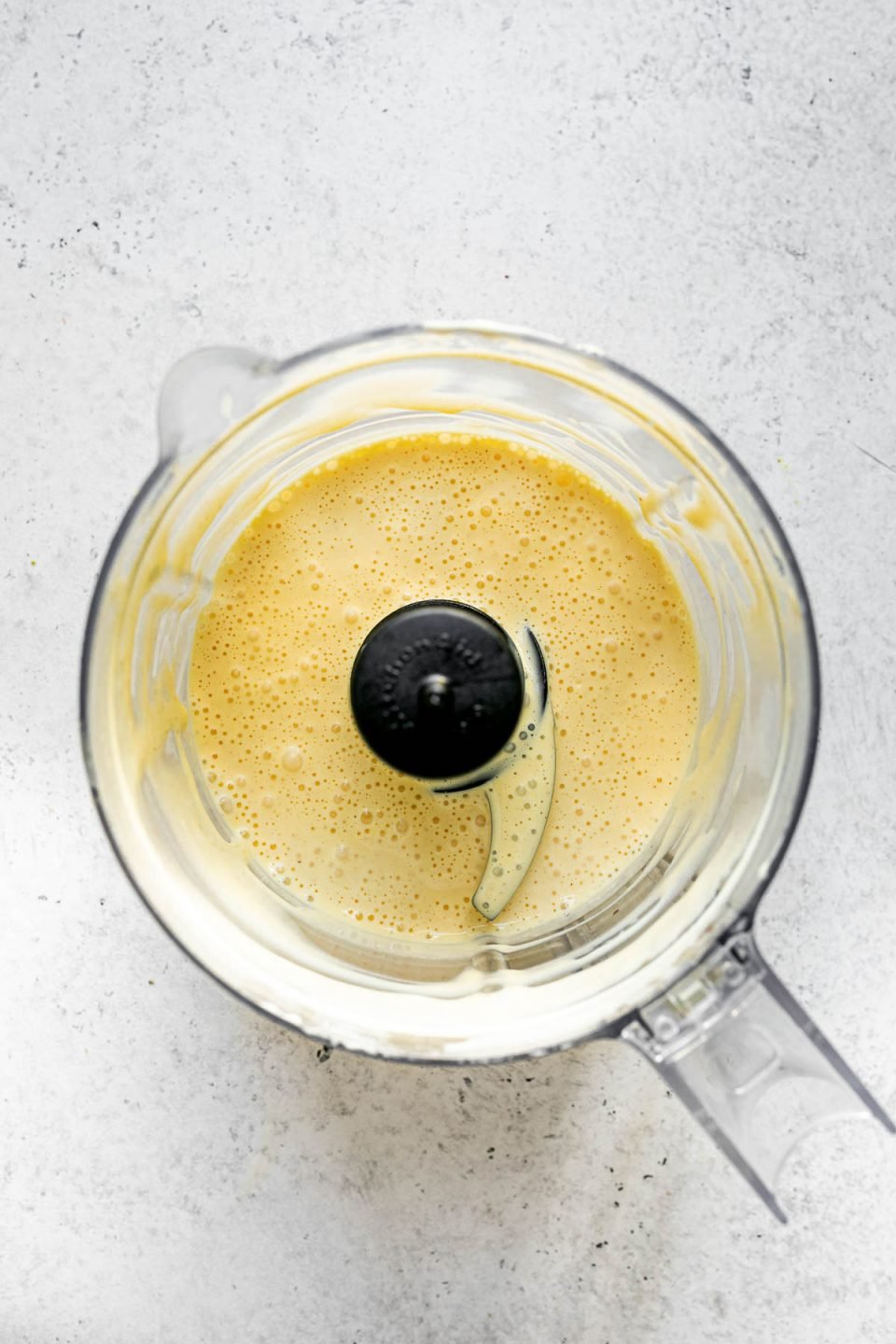 Blender hollandaise sauce in a small food processor atop a white surface.