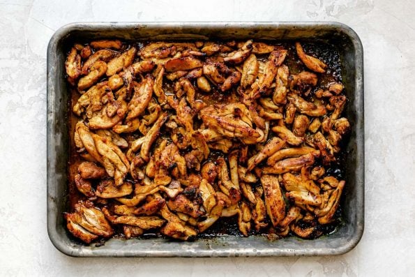Thinly sliced broiled chicken shawarma on a small baking sheet atop a creamy cement surface.