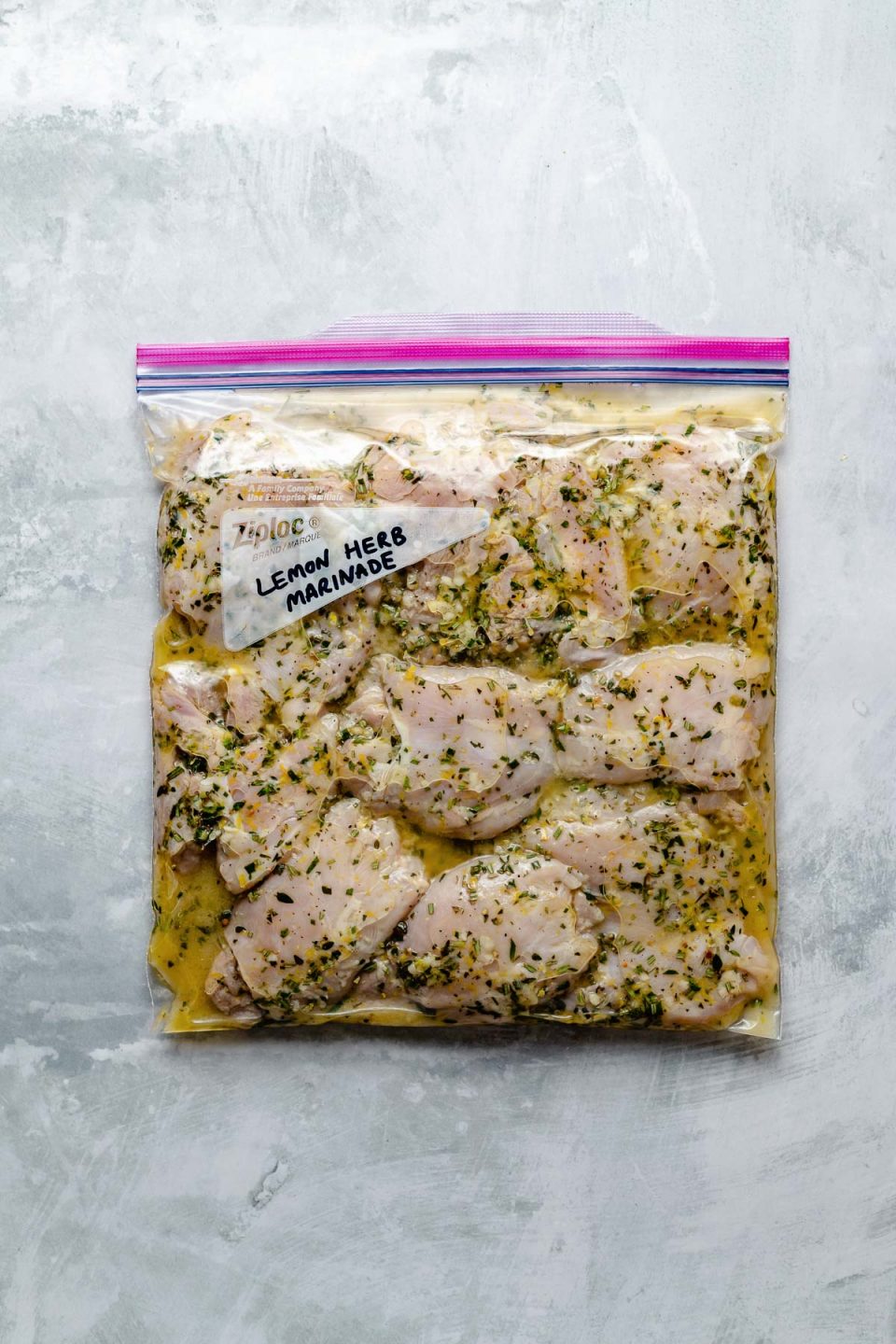 Chicken thighs in a Ziploc bag, marinating in Simple Lemon Herb marinade. The bag sits atop a light blue surface. “Lemon Herb Marinade" is penned in the bag's memo area.