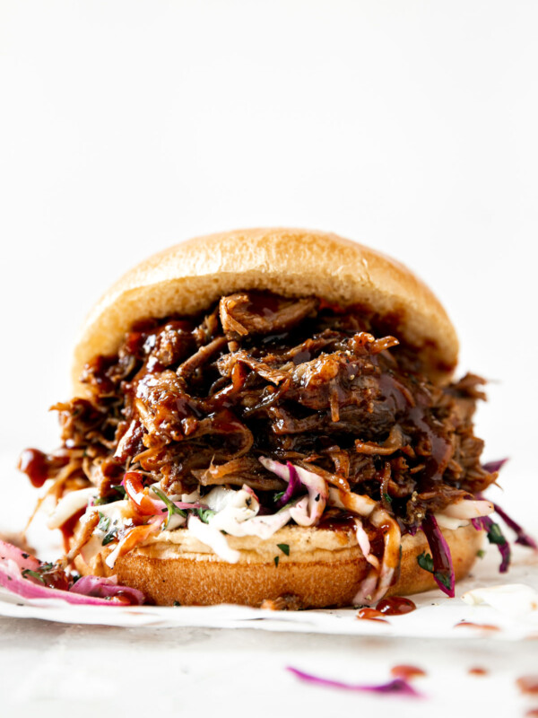 Straight-on view of pulled pork sandwich. Pulled pork & slaw on a brioche bun, atop a creamy white surface.