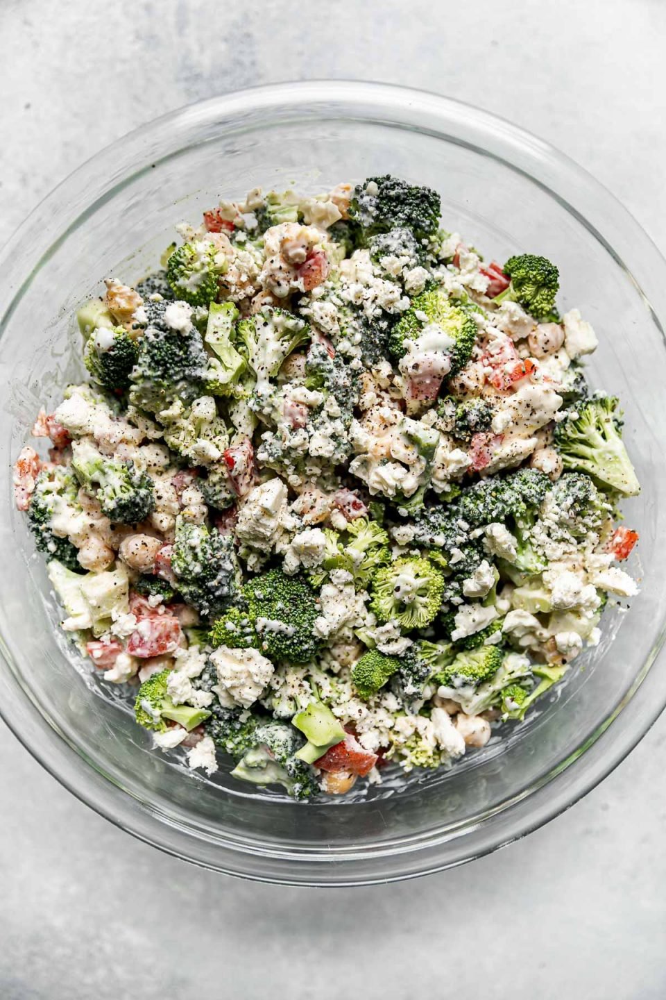 Dressed healthy broccoli salad shown in a large glass mixing bowl atop a light gray surface.