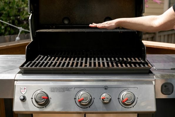 A woman's hand shown above an open Weber Genesis II, prepared for 2-zone grilling with one side of burners all the way open and the other side only part way open.