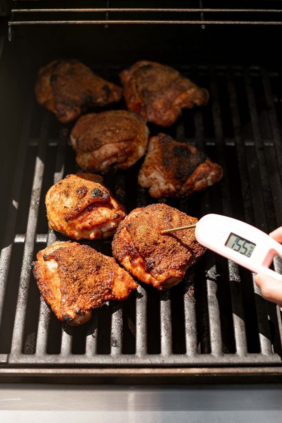 An instant-read thermometer inserted in grilled BBQ chicken thighs, with a registered temperature of 155 degrees F. 