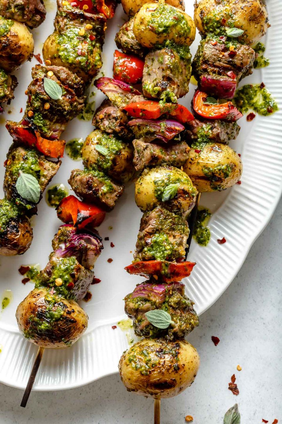 Close up of grilled steak and potato kabobs, topped with bright green chimichurri sauce.