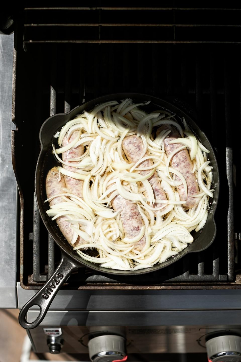 Brats, sliced onion, & beer in a large black cast iron skillet placed on the grill grates.