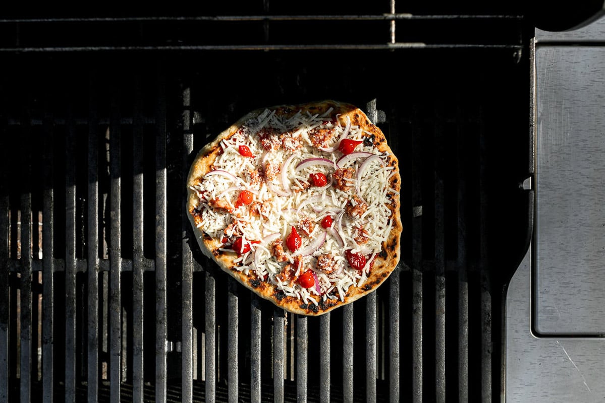 How to grill pizza, Step 6: Assembled pizza shown on grill grates over direct heat.