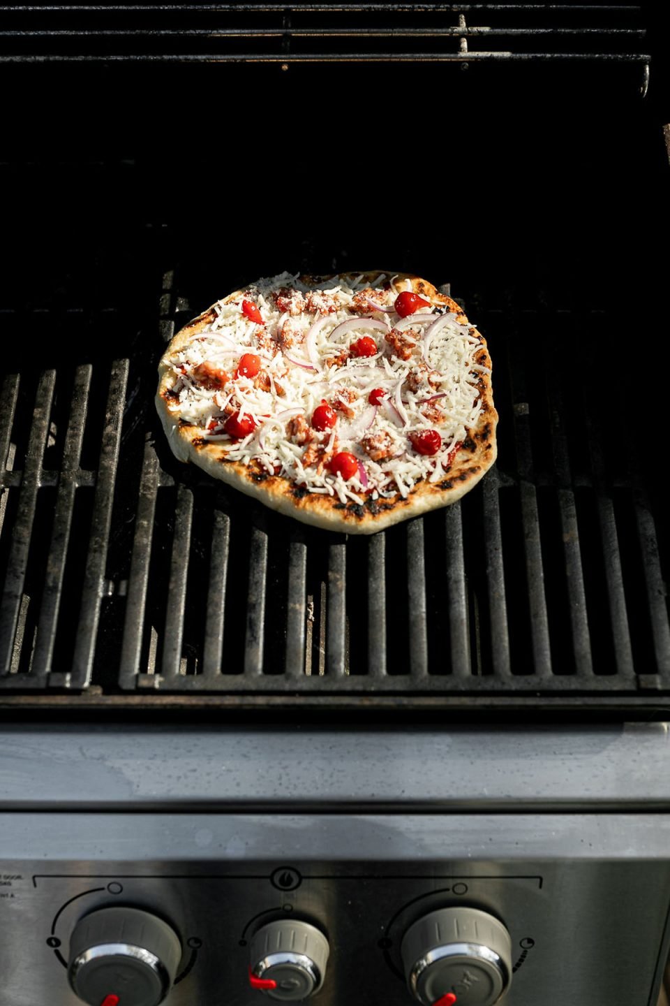 Assembled pizza shown on grill grates over direct heat.