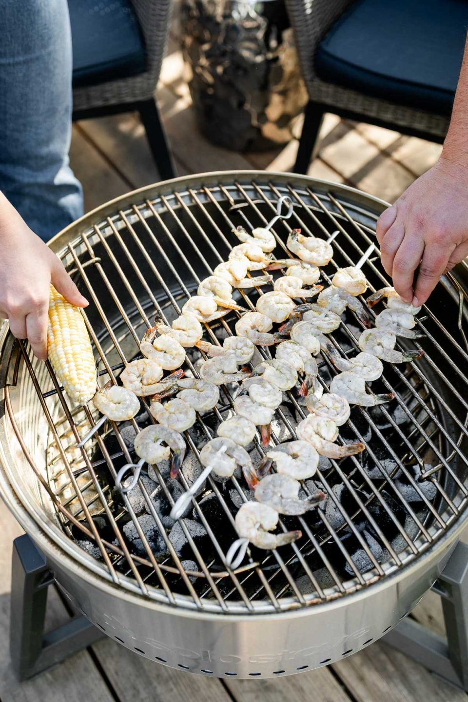 A top down shot of Jess of Plays Well With Butter and her husband Chris arranging shrimp skewers & a piece of corn on the cob on top of their Solo Stove Grill.