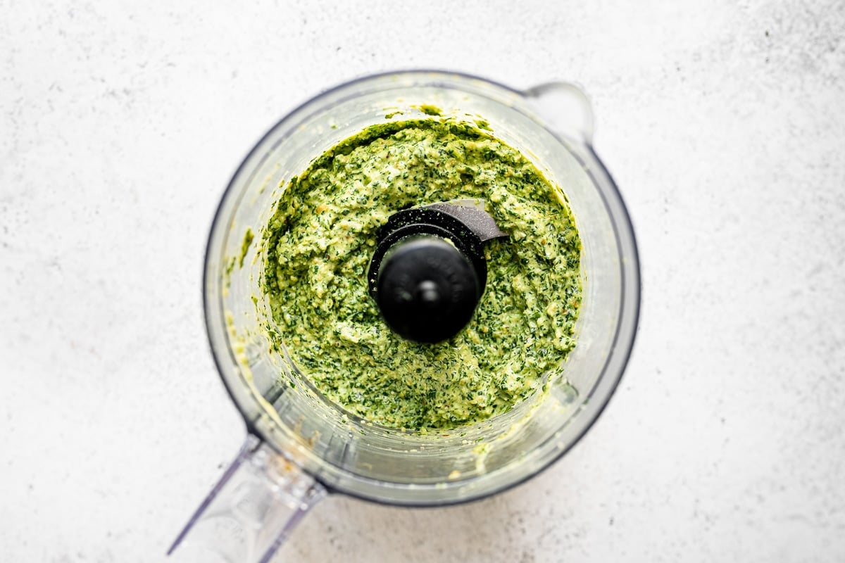 Blended jalapeño pesto in a food processor carafe, atop a light gray & white surface.