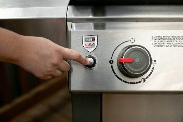 How to Start a Propane Grill, Step 3: A woman's hand presses the electric start button of a Weber Genesis II propane grill.